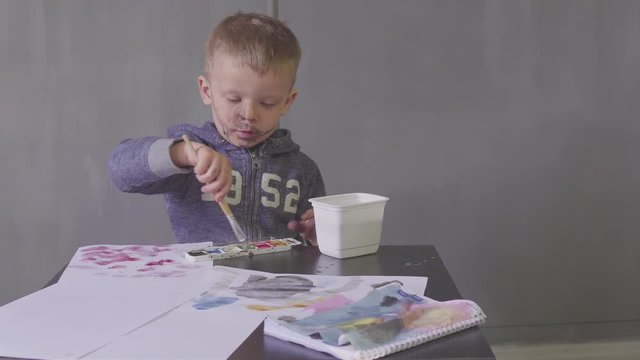 A child funny boy with cut face is drawing with colored paints