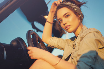 Young beautiful girl sitting in cabrio car on sunset wait for friends and think about perfect...