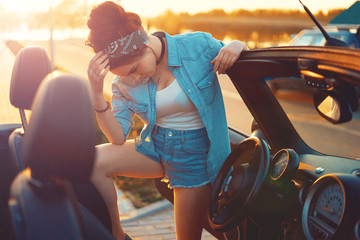 Young beautiful girl sitting in cabrio car on sunset wait for friends and think about perfect...