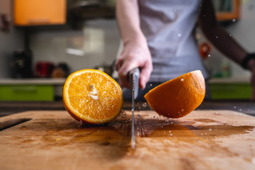 Chef cutting an orange in half with knife in motion. Splashes of water fly in different directions...