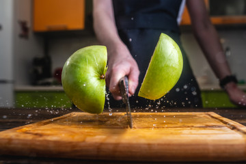 Chef cutting a green apple in half with knife. Splashes of juice fly in different directions and freeze in the air