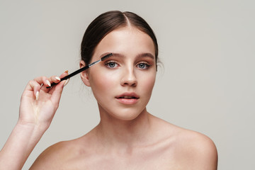 Image of beautiful young shirtless woman using eyebrows brush