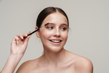 Fototapeta premium Image of joyful young shirtless woman using eyebrows brush and smiling