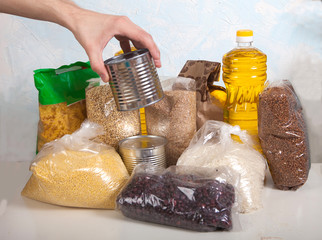 A set of products from cereals, legumes, vegetable oil and canned food on a light background. Male hand holds a can of canned food.