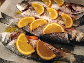 Sea bass with slices of orange in sheet pan prepared for baking in oven