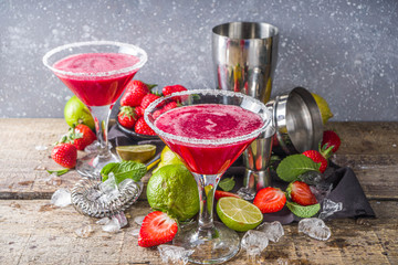 Summer cold alcohol drink. Strawberry margarita cocktail, with lime, mint and fresh strawberry on rustic wooden background