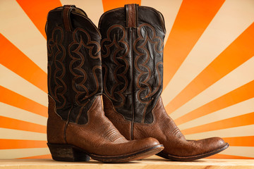 Old country western cowboy boots against a retro pop orange striped background.