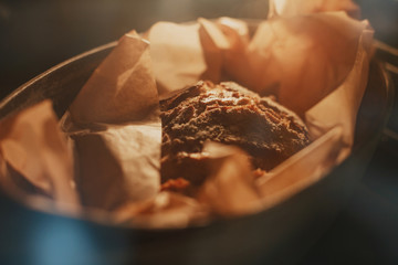 Freshly baked loaf of homemade bread wrapped in baking paper inside steel baking tray