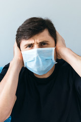 Male in blue medical face mask holding his head with his hands. Man in shock, stay at home during quarantine