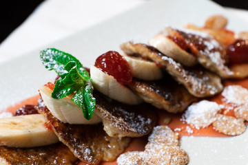 Juicy fritters with fruit for breakfast. Tasty cheesecakes with jam and bananas. Beautiful food from the restaurant cooked by a chef cook. Sweet dessert. A dish of flour and eggs.