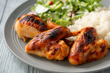 Grilled chicken wings and drumsticks, served with boiled rice and salad.
