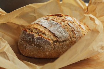Freshly baked loaf of bread with flour covered crust unwrapped from baking paper
