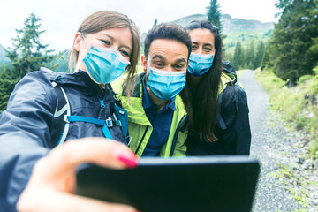 Hiking friends in protective masks standing on mountain terrain taking a selfie on a foggy day