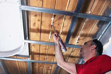 Professional worker uses mounting foam to close the cracks between boards on the ceiling