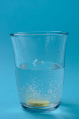 The sizzling vitamin C tablet dissolves in a transparent glass of water on a blue background