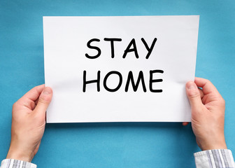 Hands of a man in a plaid shirt, holding a sheet of paper on which is written stay home. The concept of safe work from home during quarantine.