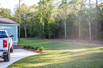 The manicured backyard of a new construction blue siding house in the suburbs with a white pickup truck parked on the driveway. © Ursula Page