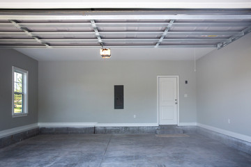 Empty large two-car garage with cement floors and a door to the inside as well as a garage door...