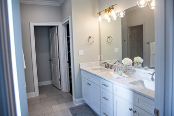 All white and gray modern contemporary master bathroom in a small new construction house with tiled floor, a vanity cabinet, double sinks and a mirror