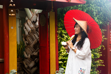 Travelers thai women wearing clothes vietnamese ethnic style with bamboo hat and red umbrella for take photo at garden and vintage retro house in resort hotel at morning time in Ratchaburi, Thailand