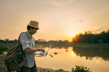  young man uses a laptop and the lake and nature at sunset