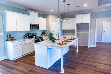 Open floor plan kitchen in a new construction empty house that has just been completed with white cabinets, pendant lighting, a bar area and hardwood floors