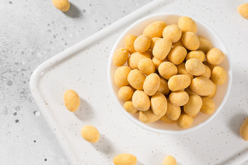 Grilled peanuts in cheese sauce in a white bowl on a light gray table. The view from the top. Close-up with space for text