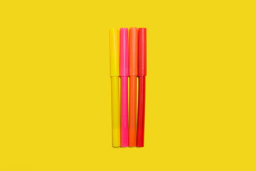 new bright plastic multicolored felt pens lying on a yellow background. concept of office supplies
