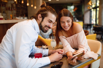 Young happy couple using smartphone in cafe