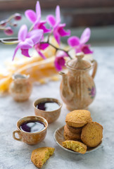 Homemade gluten-free cornmeal cookies on a light table, along with a coffee service and a yellow napkin in the background and an archidea branch
