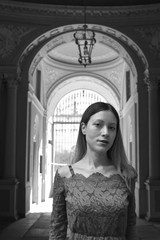 Portrait of a beautiful young woman with long hair and a lace dress with an Italian stone and marble neoclassical palace entrance in the background. Black and white.