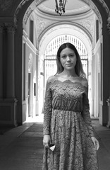 Portrait of a beautiful young woman with long hair and a lace dress with an Italian stone and marble neoclassical palace entrance in the background. Black and white.