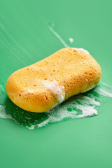 Yellow washing sponge in soap foam on a green background close up isolated