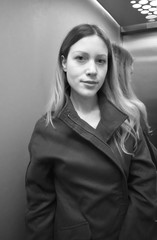 Portrait of a beautiful young woman with long hair and a black coat high-necked in a lift. Black and white.