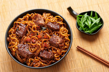 Ram-Don or Chapaguri noodles with beef steak in black bowl. Jjapaguri is a popular south korean dish with ramen and udon noodles and beef steak.