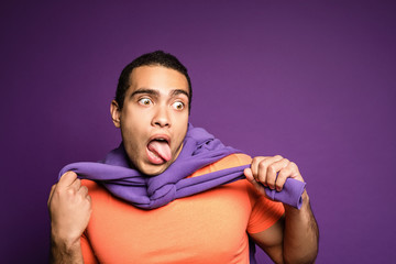 Funny face expression. Young man in bright outfit pretending he’s choking with his tongue out and...
