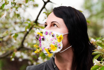 Fototapeta premium Woman in protective mask with flowers during coronavirus, pandemic and quarantine. Summer time with beautiful medical mask made from bouquet. Portrait with eyes.