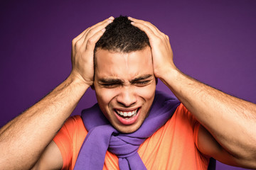 Close up portrait of young tired screaming man, holding his head with hands and having a heavy headache. Annoying noises. Not listening to anybody. Migraine. Sensitivity to sound. Nausea