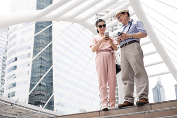 Senior Asian couple playing mobile outdoors.