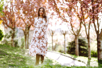 Fototapeta na wymiar Beautiful young woman near the blooming spring tree. Attractive girl enjoying her time outside in park. Spring time.
