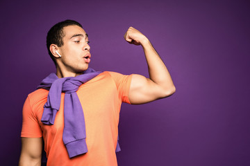 Portrait of young smiling and cheerful happy man looking at his biceps. Strong muscular body. A...