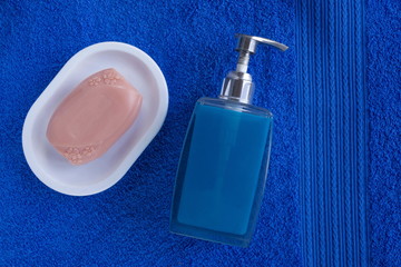 Dispenser and soap in a soap dish. Against the background of a blue terry towel