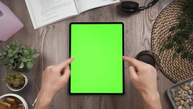 Top view on Big tab on the table with chromakey green screen on it. Hands show thumbs up. Forefingers point to screen of the tablet. Joyfully moving of hands. Daylight. 4k video.