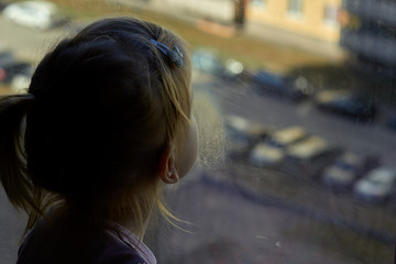 Girl looks lonely through window by putting her hands on window sill