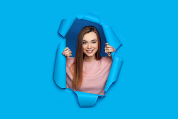 Portrait of beautiful happy smiling caucasian woman posing in blue paper hole.