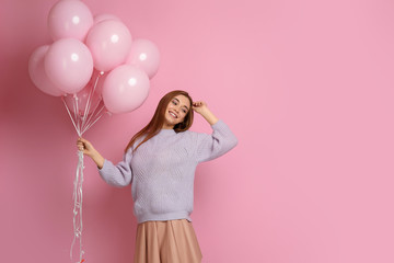 Smiling carefree caucasian girl in knitted sweater dancing with pastel pink air balloons isolated on pink background. Beautiful happy young woman on a birthday holiday. space for text