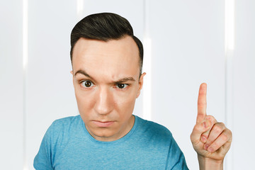 Young frowns threaten man point finger, dressed in a blue t shirt.