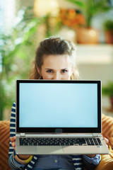 young woman sitting on couch and showing laptop blank screen