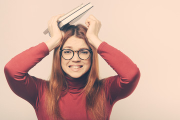 Obraz na płótnie Canvas Stressed female student with books over head. Tired young woman in eyeglasses holding textbooks and looking up isolated on white background. Education concept