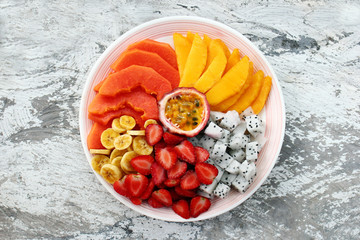 Plate with tropical fruits on a white shabby wooden background, flat lay.